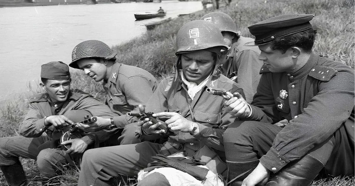 WW2 Soviet officer and US soldiers army together, examining pistols on the riverbank