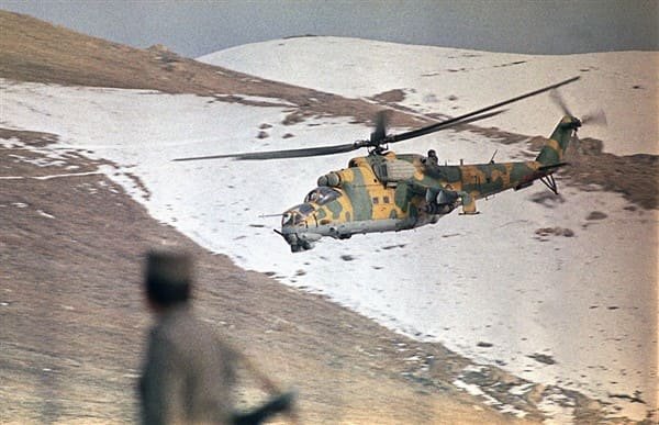 Afghan government army helicopter flying over mountains while covering a Soviet military convoy during the Afghan War in the 1980s