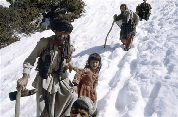 Afghan refugees walking through snow in the mountains during the 1980s Afghan war