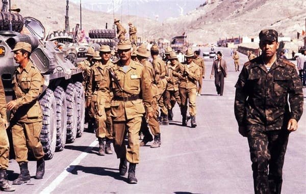 Soviet soldiers in Afghanka uniform walking beside armored vehicles during the Afghanistan War 1979-1989