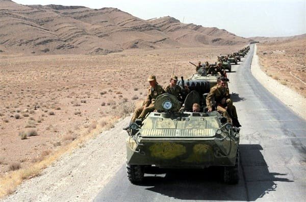 Soviet BTR armored personnel carriers driving in convoy across a desert road in Afghanistan during the 1980s war
