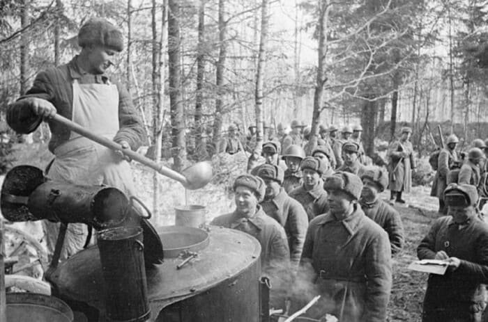Soviet field kitchen cook serving hot food to soldiers in forest during World War II