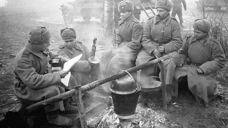 Soviet soldiers cooking food over open fire in field conditions during World War II