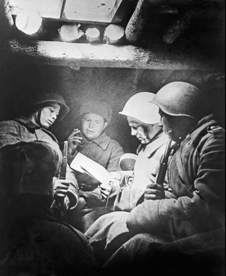 Soviet soldiers sitting inside a dugout reading a letter during wartime